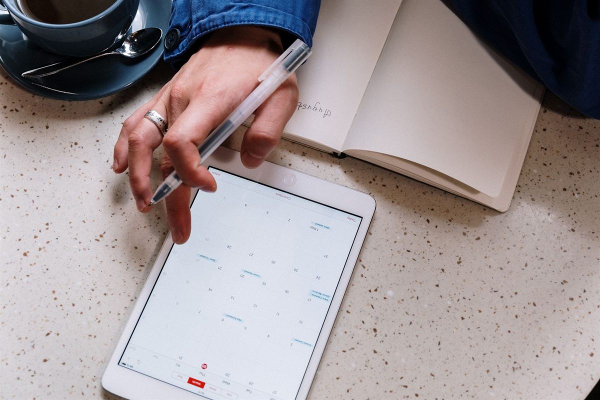 Planning on a tablet beside an open notebook and a cup of coffee